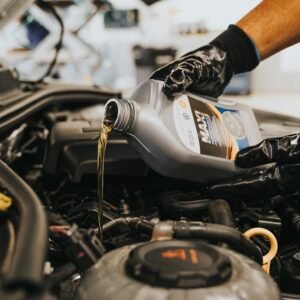 A close-up of a mechanic in gloves pouring engine oil into a car engine, showcasing automotive maintenance.